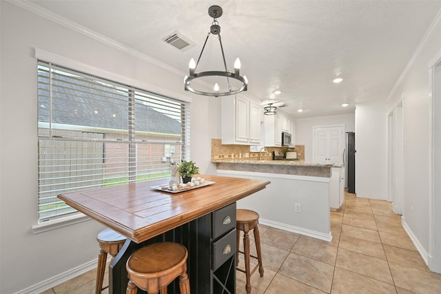 kitchen featuring pendant lighting, appliances with stainless steel finishes, white cabinetry, tasteful backsplash, and ornamental molding