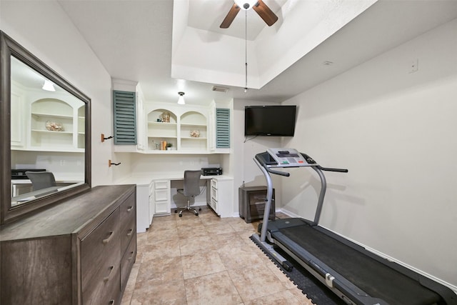 workout area with built in desk, a raised ceiling, ceiling fan, and light tile patterned flooring