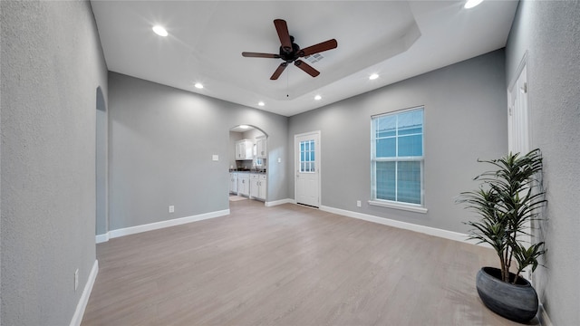 unfurnished living room with ceiling fan, a raised ceiling, and light hardwood / wood-style flooring