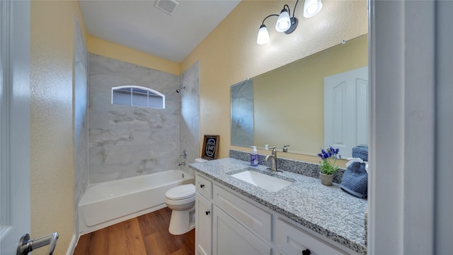 full bathroom featuring hardwood / wood-style flooring, vanity, tiled shower / bath combo, and toilet