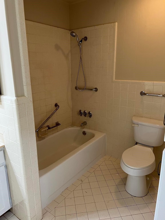 bathroom with tile patterned flooring, tiled shower / bath, tile walls, and toilet