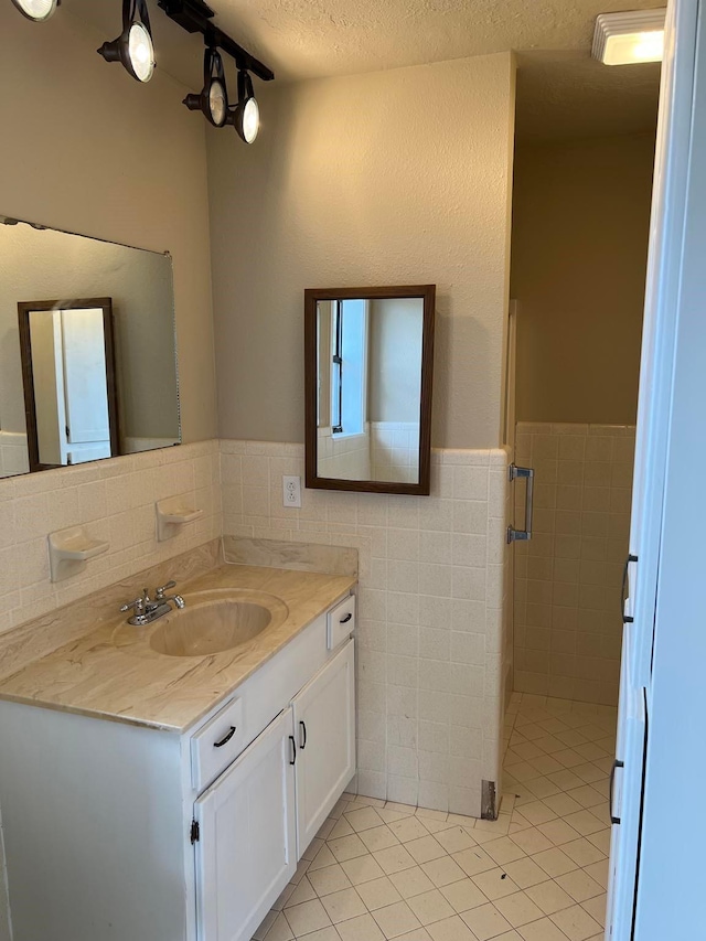 bathroom with vanity, tile patterned flooring, a textured ceiling, and tile walls