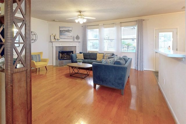 living room featuring hardwood / wood-style flooring, ceiling fan, a tile fireplace, and a textured ceiling