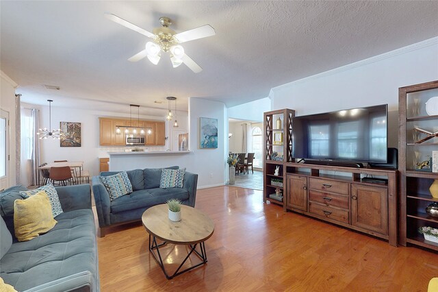 living room featuring crown molding, ceiling fan with notable chandelier, a textured ceiling, and light hardwood / wood-style flooring