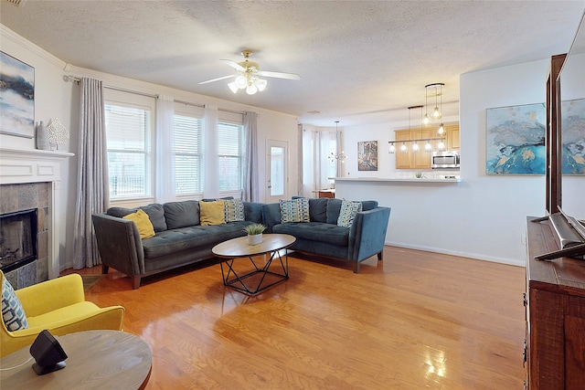 living room featuring a tiled fireplace, ceiling fan, a textured ceiling, and light hardwood / wood-style flooring