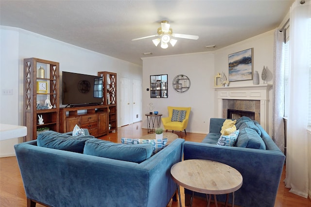 living room featuring hardwood / wood-style floors, crown molding, a tile fireplace, and ceiling fan