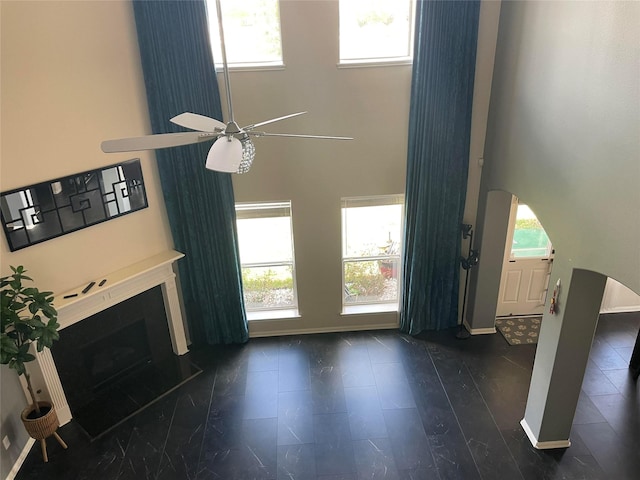 unfurnished living room featuring ceiling fan, a healthy amount of sunlight, dark hardwood / wood-style floors, and a towering ceiling