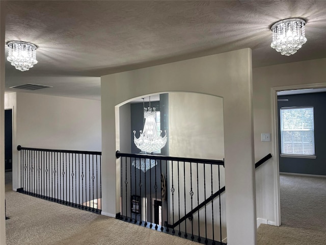 corridor with carpet flooring, a textured ceiling, and a notable chandelier