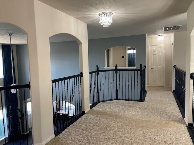 corridor with an inviting chandelier, carpet, and a textured ceiling