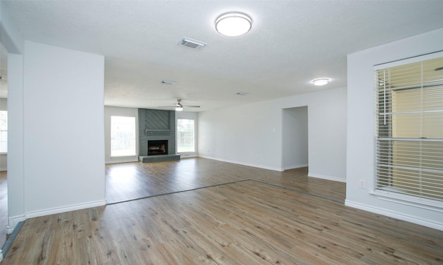 unfurnished living room with a fireplace, a textured ceiling, wood-type flooring, and ceiling fan