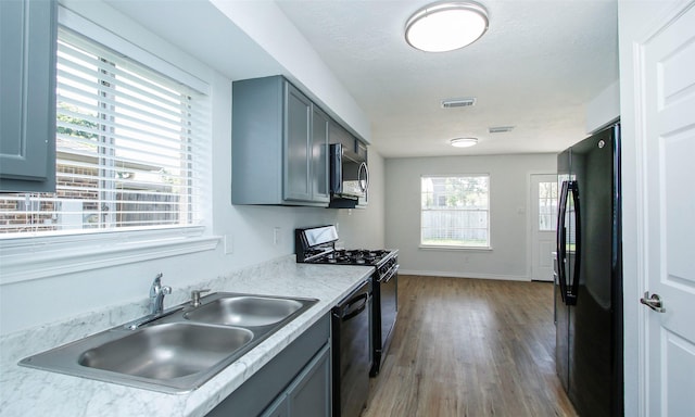 kitchen featuring hardwood / wood-style flooring, gray cabinets, sink, and black appliances