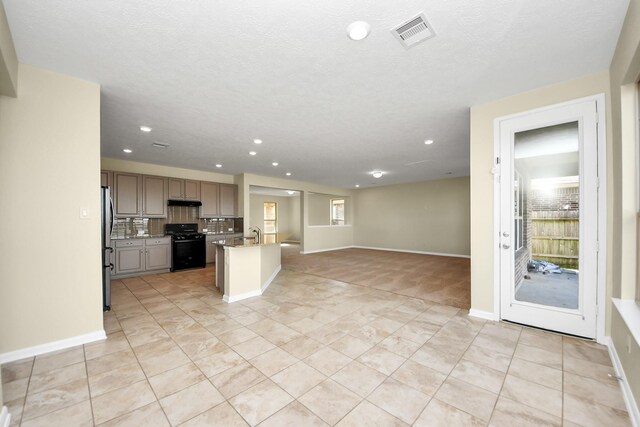 kitchen with gray cabinets, black stove, stainless steel refrigerator, an island with sink, and decorative backsplash