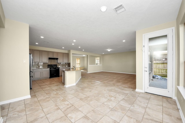 kitchen featuring gray cabinets, black range oven, stainless steel refrigerator, an island with sink, and decorative backsplash