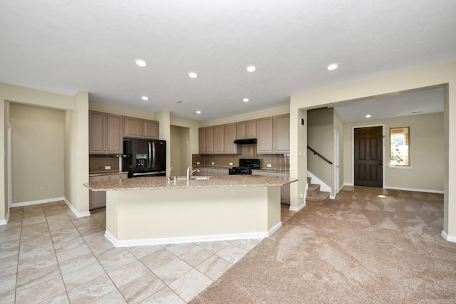 kitchen featuring sink, light stone counters, a kitchen island with sink, decorative backsplash, and black appliances