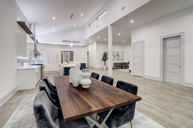 dining room featuring high vaulted ceiling and light hardwood / wood-style flooring