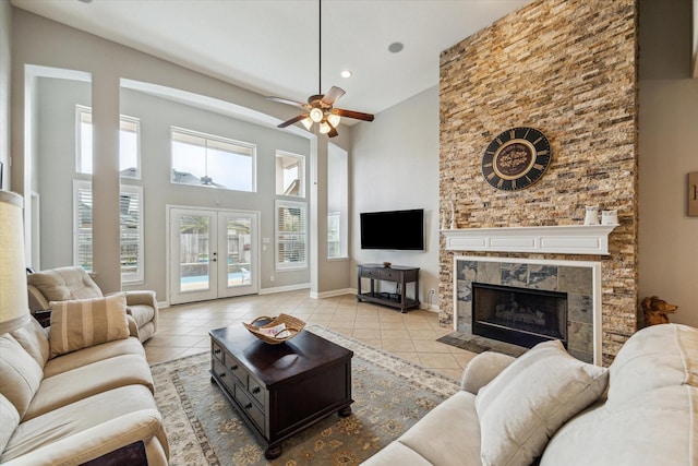 tiled living room featuring a high ceiling, ceiling fan, a fireplace, and french doors