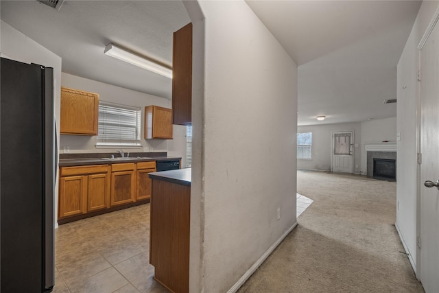 kitchen with sink, stainless steel refrigerator, dishwasher, a tiled fireplace, and light colored carpet