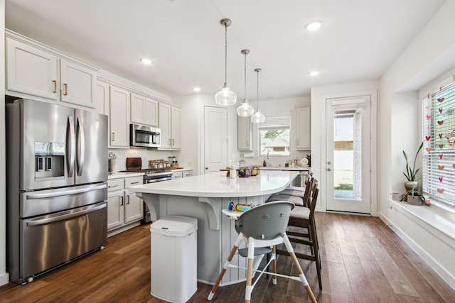 kitchen with a kitchen island, decorative light fixtures, white cabinets, a kitchen bar, and stainless steel appliances