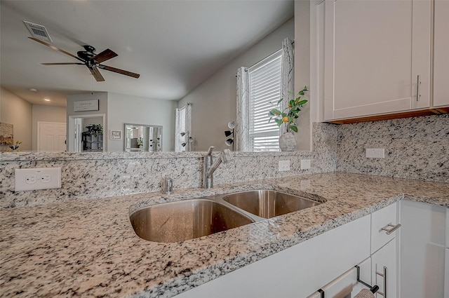 kitchen with sink, ceiling fan, white cabinetry, backsplash, and light stone counters