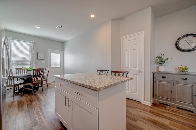 kitchen with white cabinetry, a center island, stainless steel fridge, and light hardwood / wood-style floors