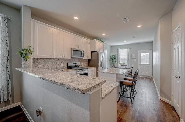 kitchen with appliances with stainless steel finishes, a kitchen bar, kitchen peninsula, and white cabinets