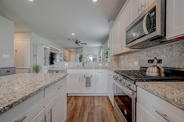 kitchen featuring sink, appliances with stainless steel finishes, light stone countertops, light hardwood / wood-style floors, and white cabinets