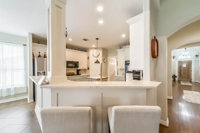 kitchen with pendant lighting, a breakfast bar area, black appliances, white cabinets, and kitchen peninsula