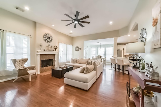 living room featuring hardwood / wood-style flooring, ceiling fan, a tile fireplace, and ornate columns