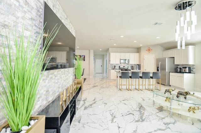 interior space featuring sink, appliances with stainless steel finishes, tasteful backsplash, white cabinets, and decorative light fixtures