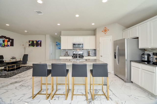 kitchen featuring white cabinetry, appliances with stainless steel finishes, a center island with sink, and dark stone counters