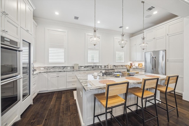 kitchen with appliances with stainless steel finishes, white cabinetry, hanging light fixtures, a kitchen breakfast bar, and a center island