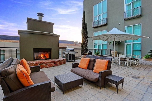 patio terrace at dusk with grilling area and an outdoor living space with a fireplace