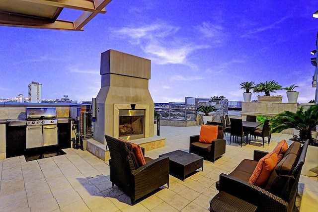 patio terrace at dusk featuring an outdoor kitchen, an outdoor fireplace, and area for grilling