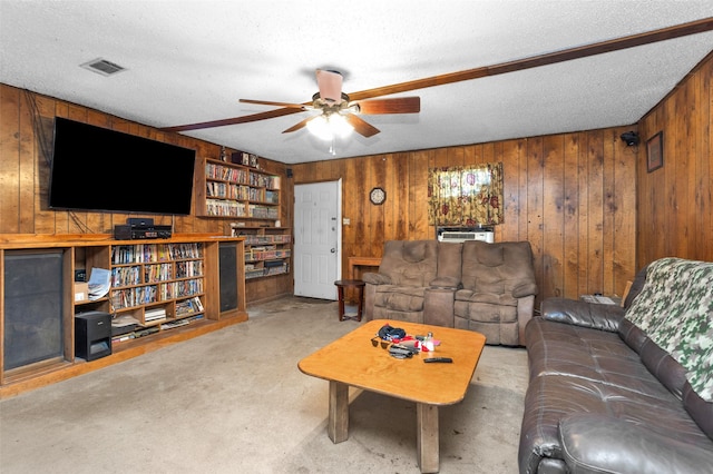 carpeted living room featuring ceiling fan, wooden walls, and a textured ceiling