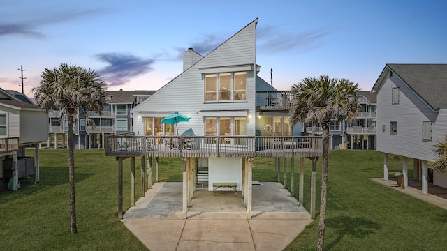 back house at dusk featuring a lawn, a carport, and a balcony