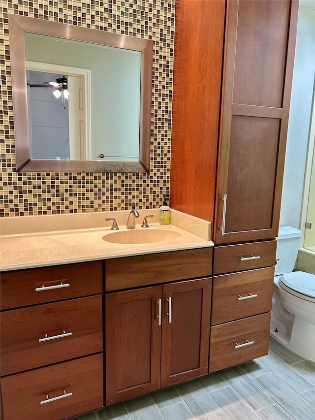 bathroom featuring ceiling fan, vanity, toilet, and decorative backsplash