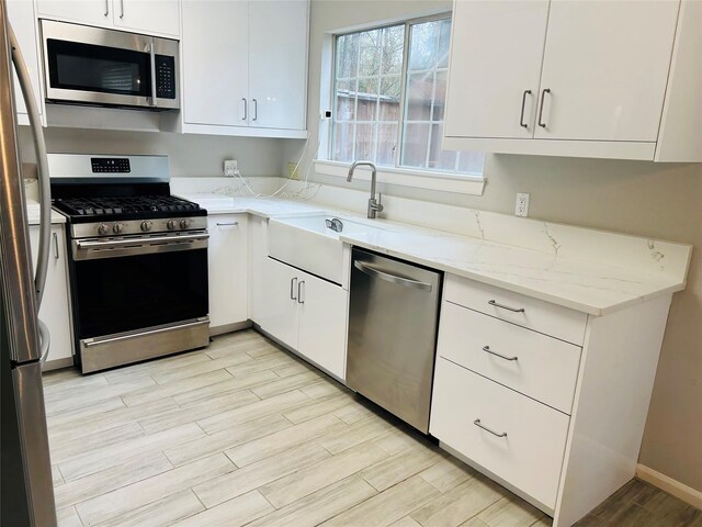 kitchen featuring appliances with stainless steel finishes, sink, white cabinets, and light stone counters