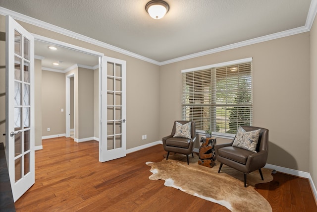 sitting room with wood finished floors, french doors, crown molding, a textured ceiling, and baseboards