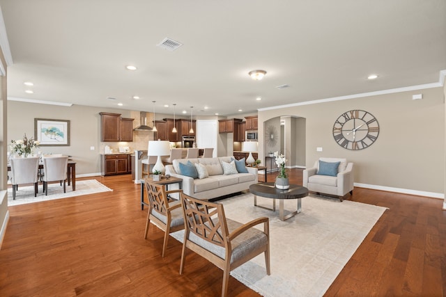 living area with crown molding, visible vents, baseboards, arched walkways, and recessed lighting