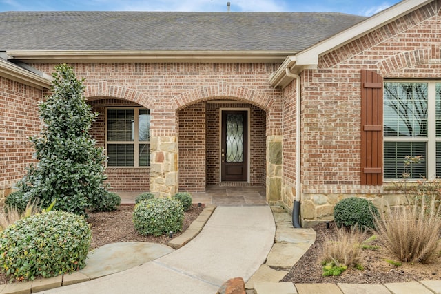doorway to property featuring brick siding and a shingled roof