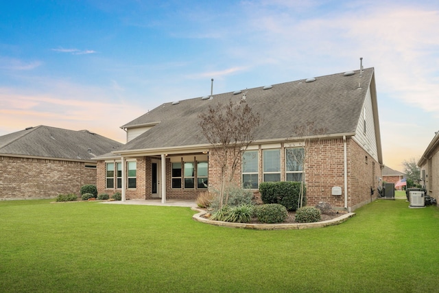 back of property at dusk with a patio area, cooling unit, brick siding, and a lawn