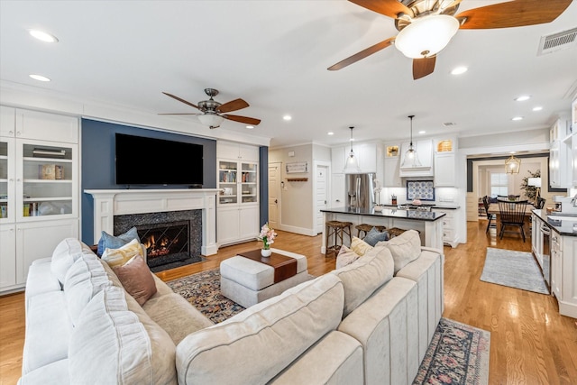 living room featuring built in shelves, ornamental molding, light hardwood / wood-style floors, and ceiling fan