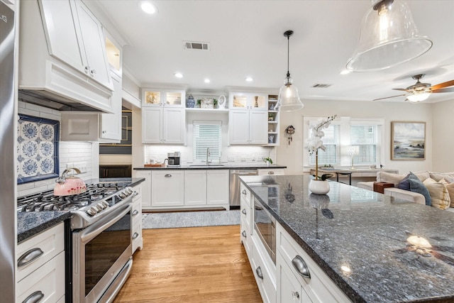 kitchen with sink, appliances with stainless steel finishes, white cabinets, decorative light fixtures, and light wood-type flooring