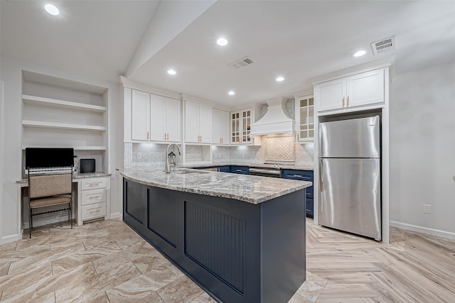 kitchen with premium range hood, white cabinetry, light stone counters, stainless steel refrigerator, and kitchen peninsula