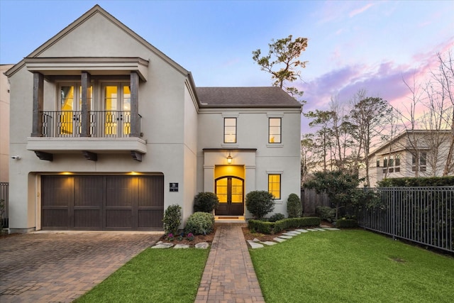 view of front of home with a garage, a lawn, french doors, and a balcony