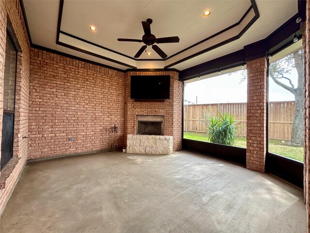 unfurnished sunroom featuring a wealth of natural light, a raised ceiling, a fireplace, and ceiling fan