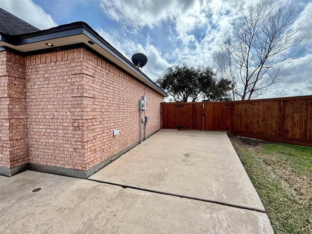 view of property exterior with brick siding, a gate, fence, and a patio