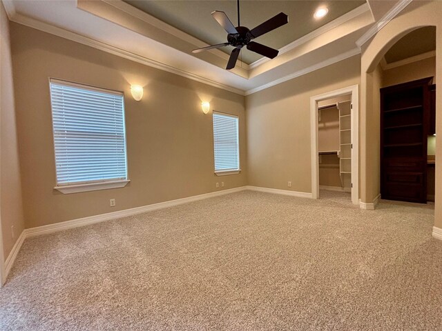 unfurnished bedroom featuring baseboards, a tray ceiling, a walk in closet, and light colored carpet