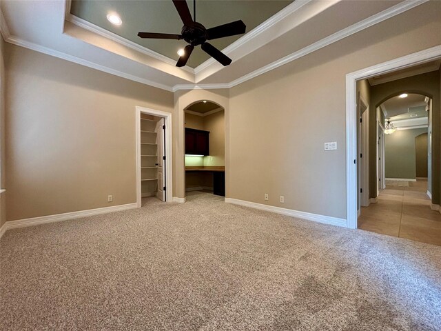 unfurnished bedroom featuring arched walkways, a walk in closet, crown molding, and light colored carpet