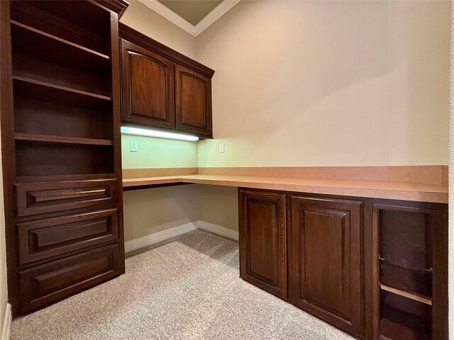 unfurnished office featuring light carpet, baseboards, built in study area, and crown molding